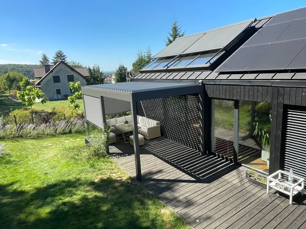 Antracytowa pergola z dachem lamelowym i boczną osłoną screen nad drewnianym tarasem